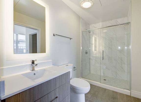 A bathroom with a toilet, sink, mirror, and shower.
