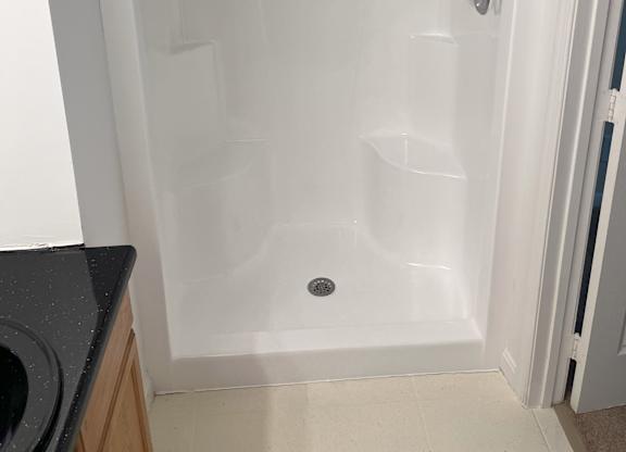 A white shower stall with a door and a drain at Shenandoah Station Apartments, Triangle, 22172