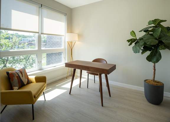 A room with a yellow chair, a brown table, and a potted plant.