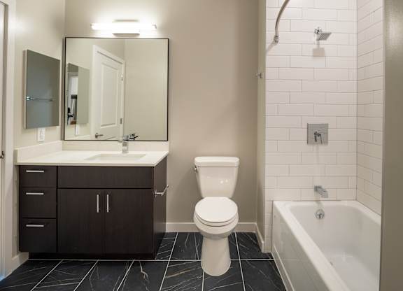 A white toilet sits in a bathroom next to a sink and a bathtub.