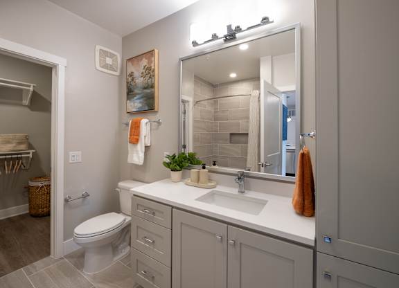 A bathroom with a toilet, sink, and mirror at The Sully Apartments, Chantilly 20151