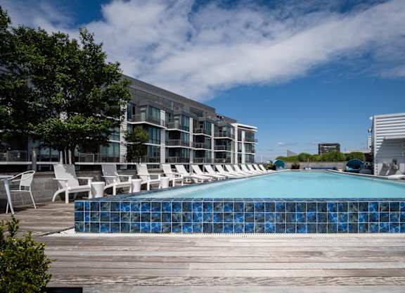 A swimming pool surrounded by white chairs and a modern building in the background. at Dock 79, District of Columbia