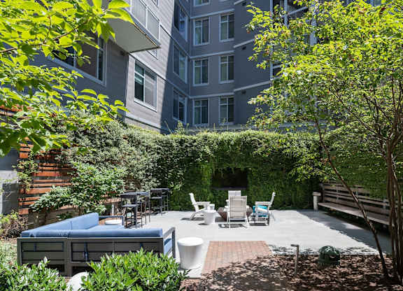 A patio with a couch, chairs, and a table surrounded by greenery. at Dock 79, Washington, 20003