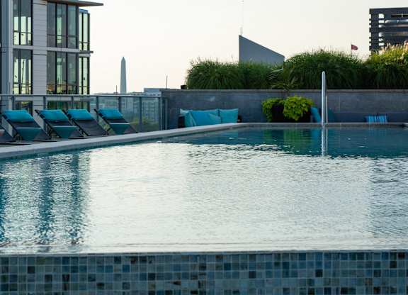 A pool with blue tiles and lounge chairs is surrounded by a concrete wall and green plants. at Dock 79, District of Columbia, 20003