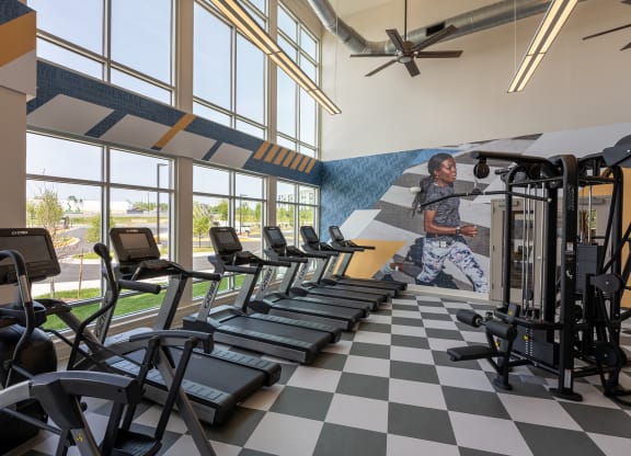 a woman runs on a treadmill in front of a wall of windows with a mural of a  at Woodmore Grand, Bowie, 20721