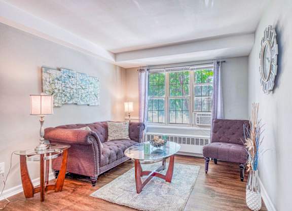 A living room with a purple couch, a glass table, and a clock on the wall at Huntwood Courts Apartments, Washington