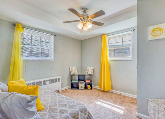 A bedroom with a bed, a ceiling fan, and yellow curtains at Huntwood Courts Apartments, Washington, DC, 20019