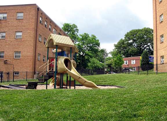 A playground with a yellow slide in front of a brick building at Huntwood Courts Apartments, Washington, Washington DC