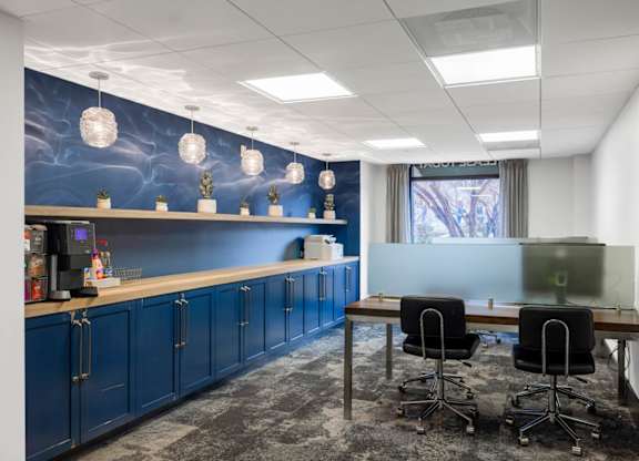 A room with a desk, chairs and a blue wall with a mural.