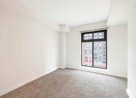 A room with a carpeted floor and a window showing a building outside.