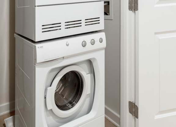 A white front loading washing machine is stacked on top of a smaller white dishwasher.