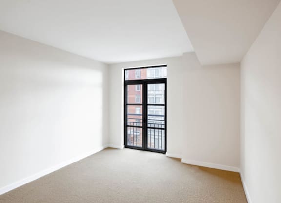 A room with a carpeted floor and a window with a view of a building outside.