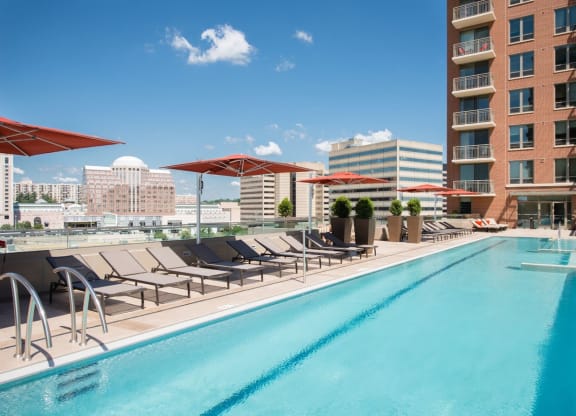 a swimming pool with lounge chairs and umbrellas next to a tall building at The Acadia at Metropolitan Park, Arlington, VA