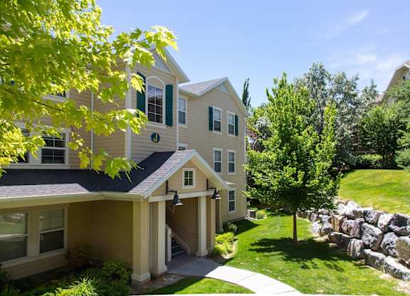 A house with a stone wall and a tree in front. at Bluffs Apartments, Utah, 84065