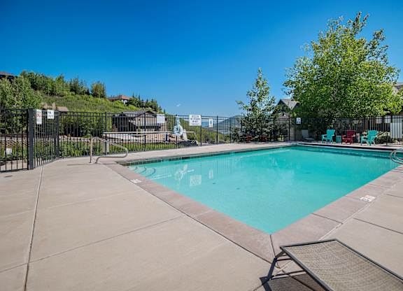 A large outdoor swimming pool surrounded by a fence and lounge chairs.at Todd Hollow at Deer Mtn., Hideout, UT  