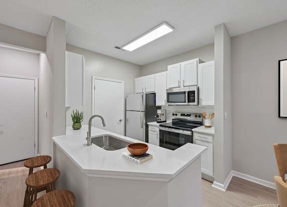 A kitchen with white cabinets and appliances, a sink, and a counter with a bowl and a book on it.