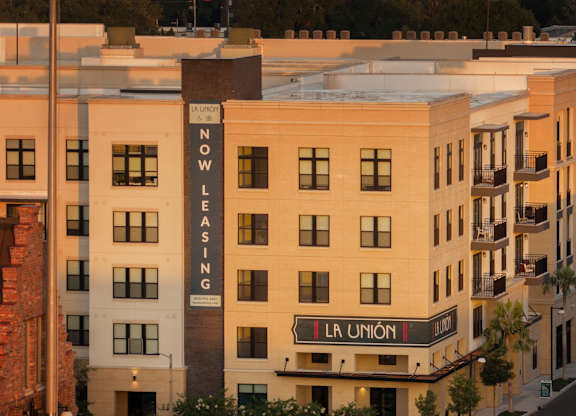 A building with a sign that says "Now Leasing" is in the foreground with an American flag flying in the background.