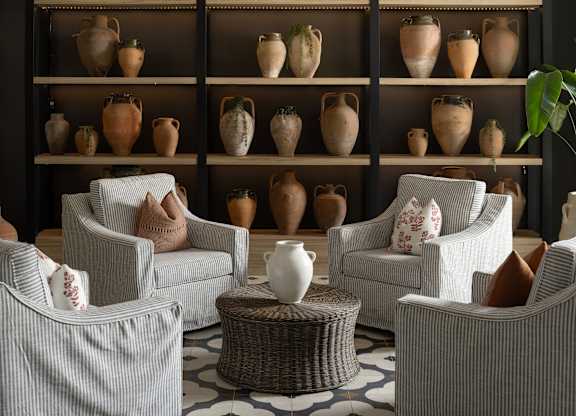 A room with a shelf full of vases and chairs.