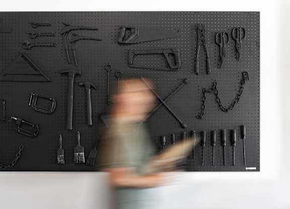 A man is walking past a wall of tools.