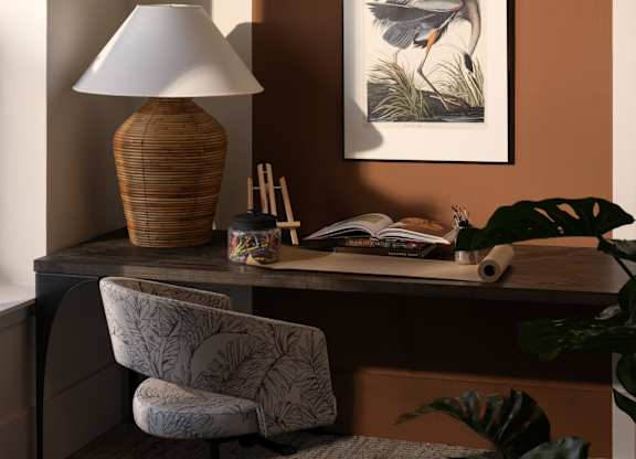A desk with a lamp, chair, and a painting of a bird.