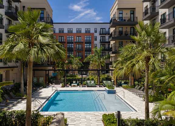 A swimming pool surrounded by palm trees and apartment buildings.