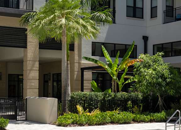 A pool surrounded by plants and trees in front of a building.