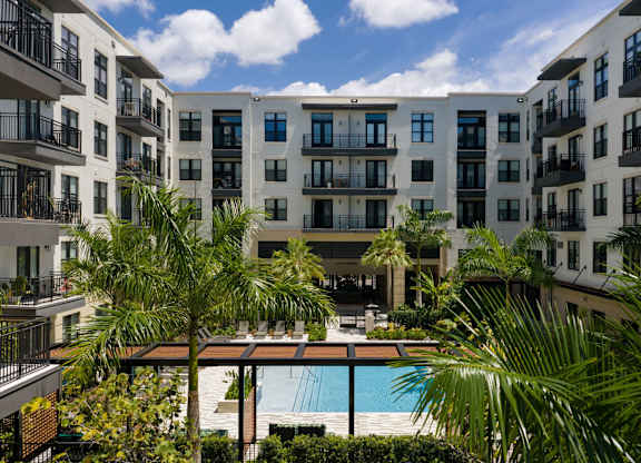 A view of a pool surrounded by palm trees and apartment buildings.