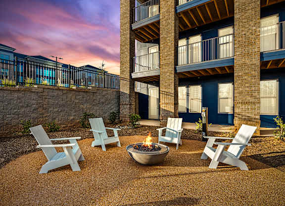 A fire pit sits in the middle of a gravel patio surrounded by four chairs.