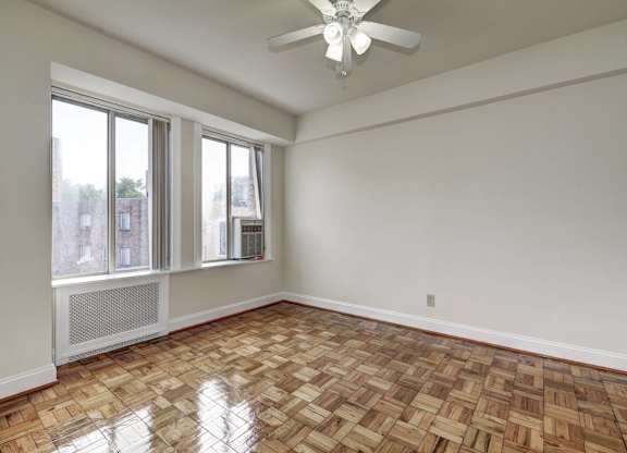 A room with a ceiling fan and a window with a view of a city.