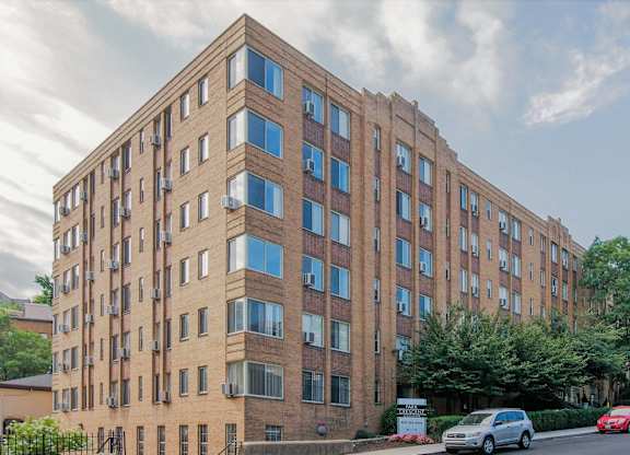 A tall brick building with many windows and cars parked in front.