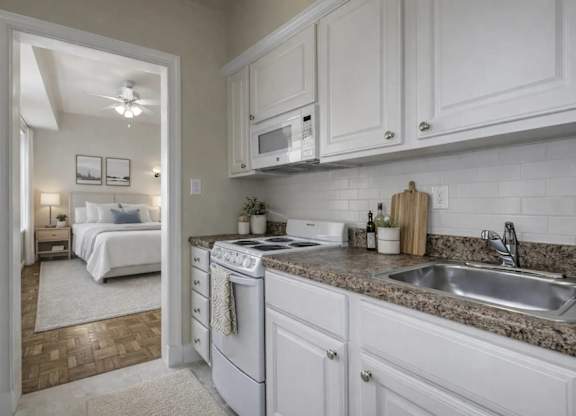 A kitchen with white cabinets and a view into a bedroom.