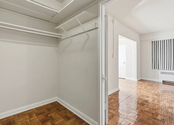 A room with white walls and wooden flooring with a doorway leading to another room.