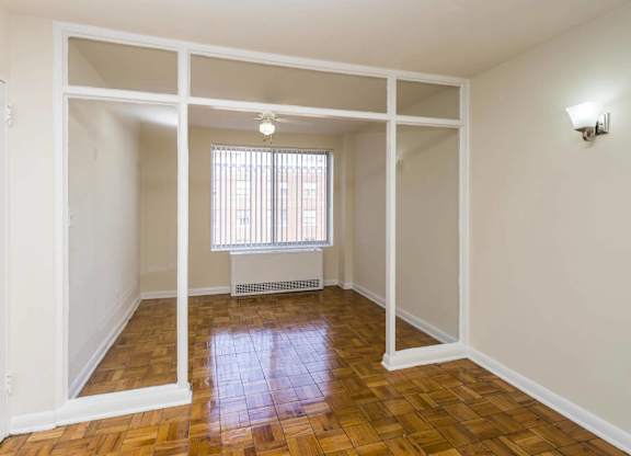 A room with white walls and wooden flooring with a window.