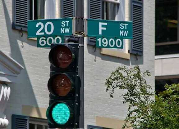 A traffic light with a green light on and street signs for 20th and F streets.