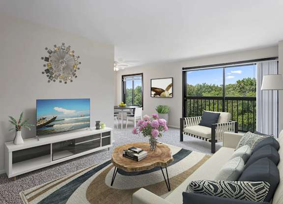 A living room with a television, a sofa, a coffee table, and a balcony with a view of the trees.