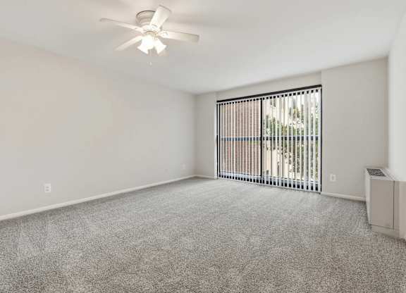 A room with a ceiling fan and a window with blinds.