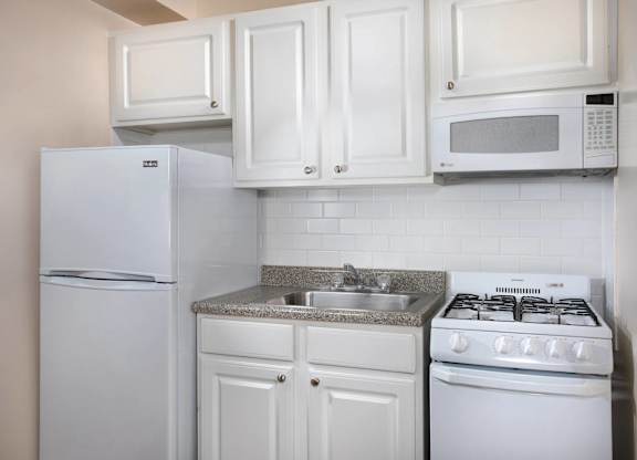 A white kitchen with a refrigerator, microwave, oven, and sink.