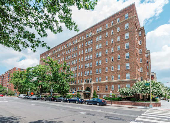 A large red brick building with many windows sits on a street corner.