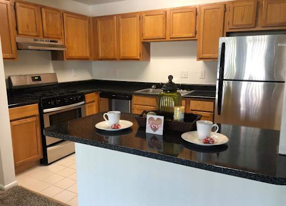 A kitchen with wooden cabinets and a black countertop at Shenandoah Station Apartments, Virginia
