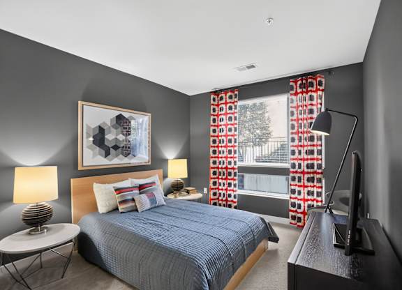 A bedroom with a bed, nightstand, and a window with red curtains.