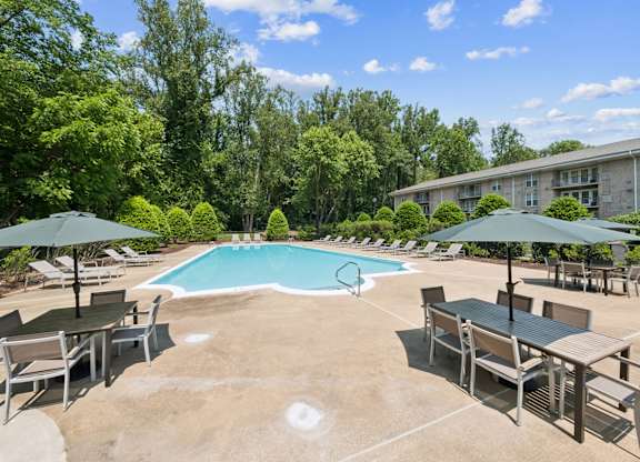 A pool surrounded by trees and chairs.