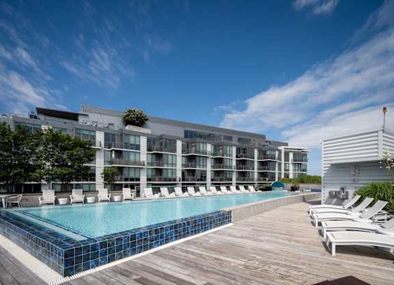 A large swimming pool with a wooden deck and lounge chairs in front of a modern building. at Dock 79, Washington, DC