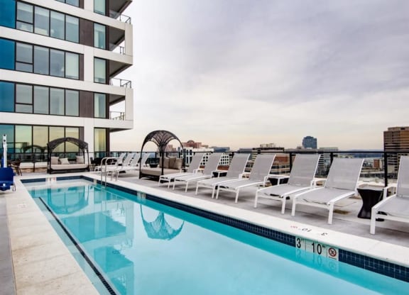 a swimming pool with white lounge chairs and a building in the background at The Boro, Tysons, VA