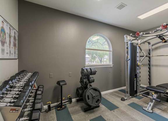 A gym with a variety of equipment including a rowing machine, a leg press machine, and a cable machine at West Park Apartments, Albuquerque