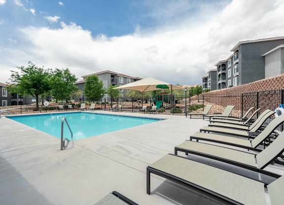 A swimming pool surrounded by sun loungers and trees at West Park Apartments, Albuquerque