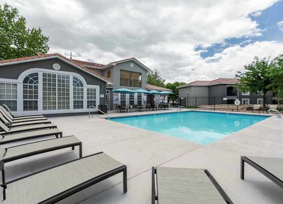 A pool area with sun loungers and a building in the background at West Park Apartments, Albuquerque
