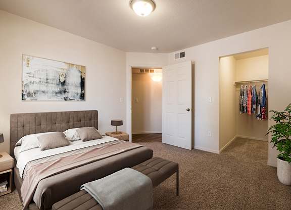 A bedroom with a bed, a bench, and a plant at West Park Apartments, Albuquerque, 87114