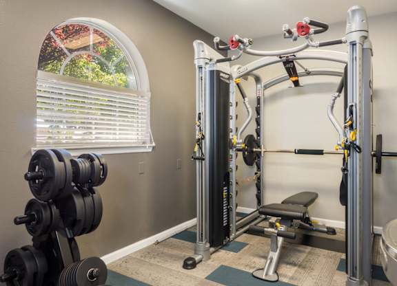 A home gym with a squat rack, bench, and weights at West Park Apartments, New Mexico 87114