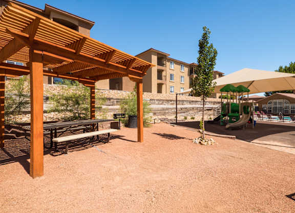 A wooden pergola is in the foreground of a sandy area with a building in the background at West Park Apartments, Albuquerque, New Mexico