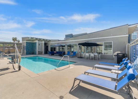 a swimming pool with lounge chairs and umbrellas in front of a building at Loma Villas Apartments, San Bernardino, CA